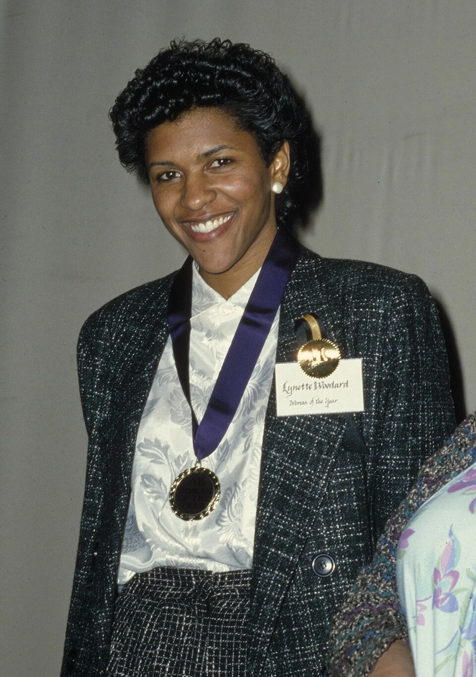 Lynette Woodard at the Ms. Magazine Woman of the Year Awards, smiling in formal attire with a medal around her neck.