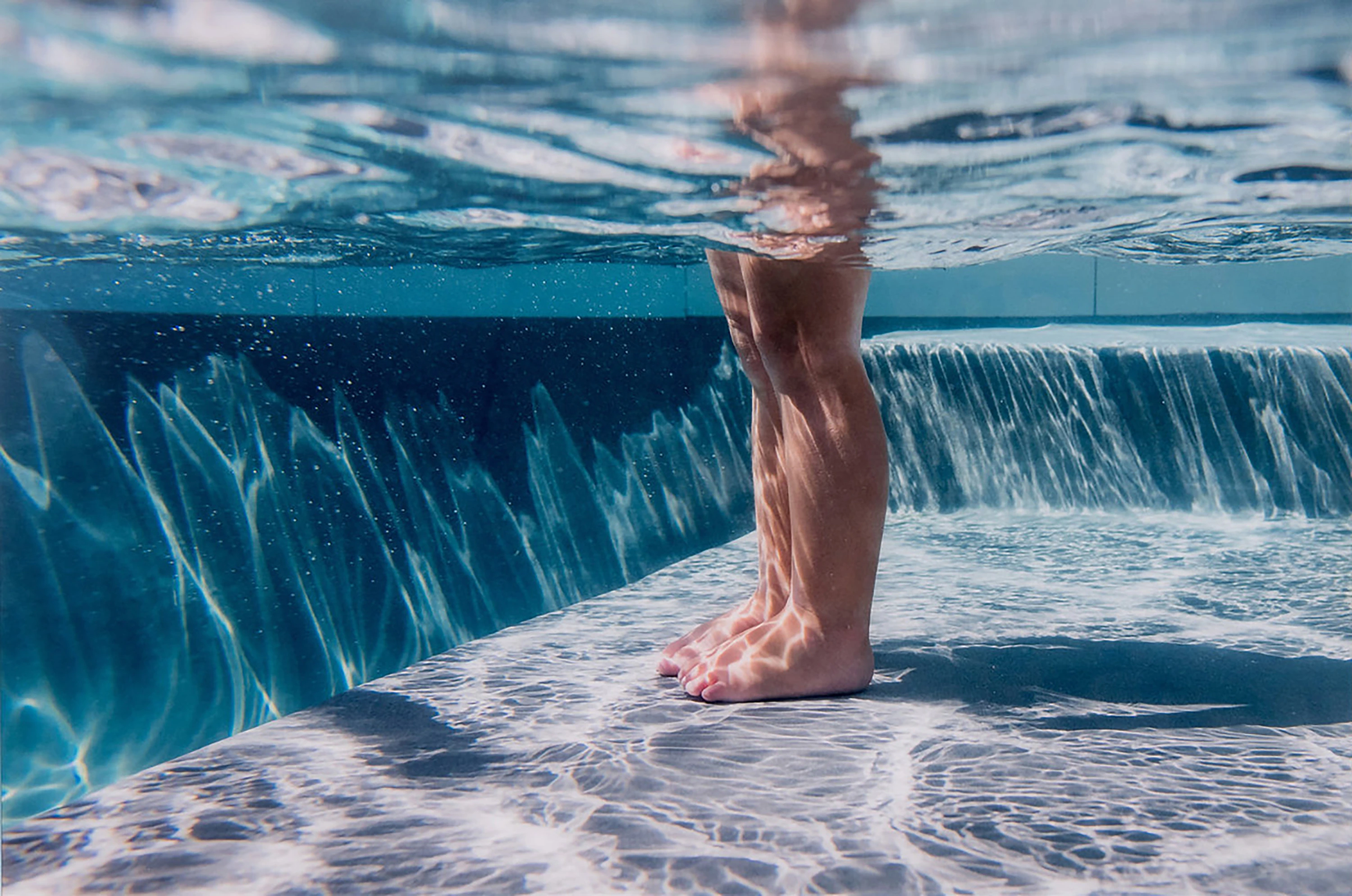 Underwater-style photograph of legs standing in a pool with rippling blue water
