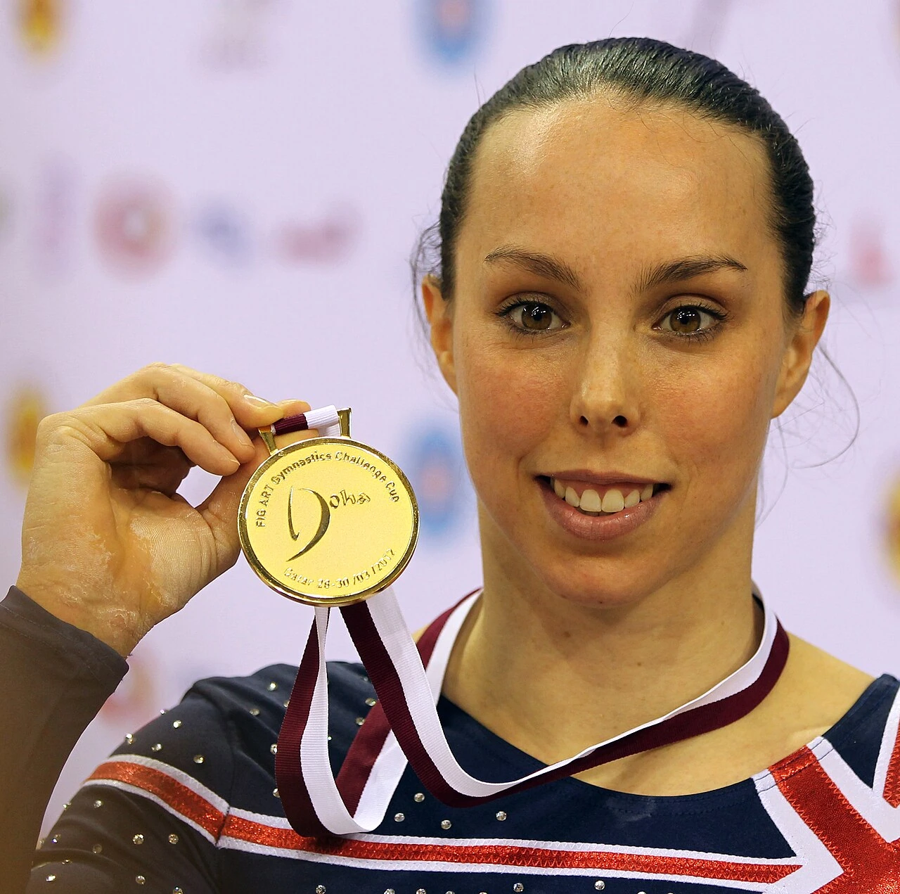 Beth Tweddle holding a gold medal and smiling at a gymnastics event