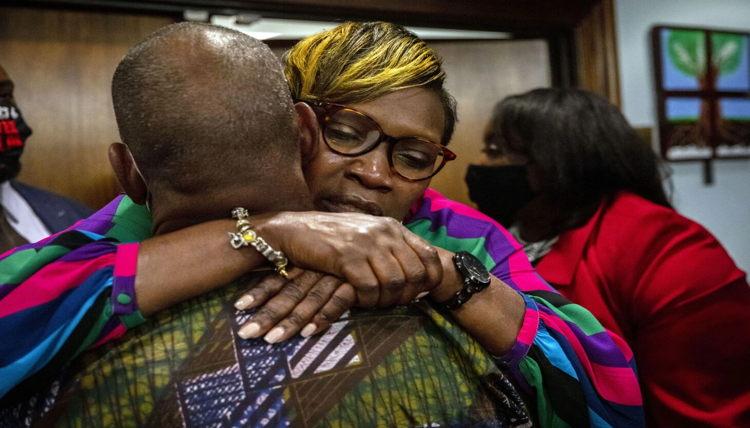 Wanda Cooper-Jones embraces someone in a courtroom, wearing glasses and a colorful striped top.
